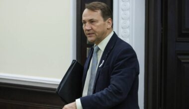 Mężczyzna w garniturze i krawacie trzyma teczkę.