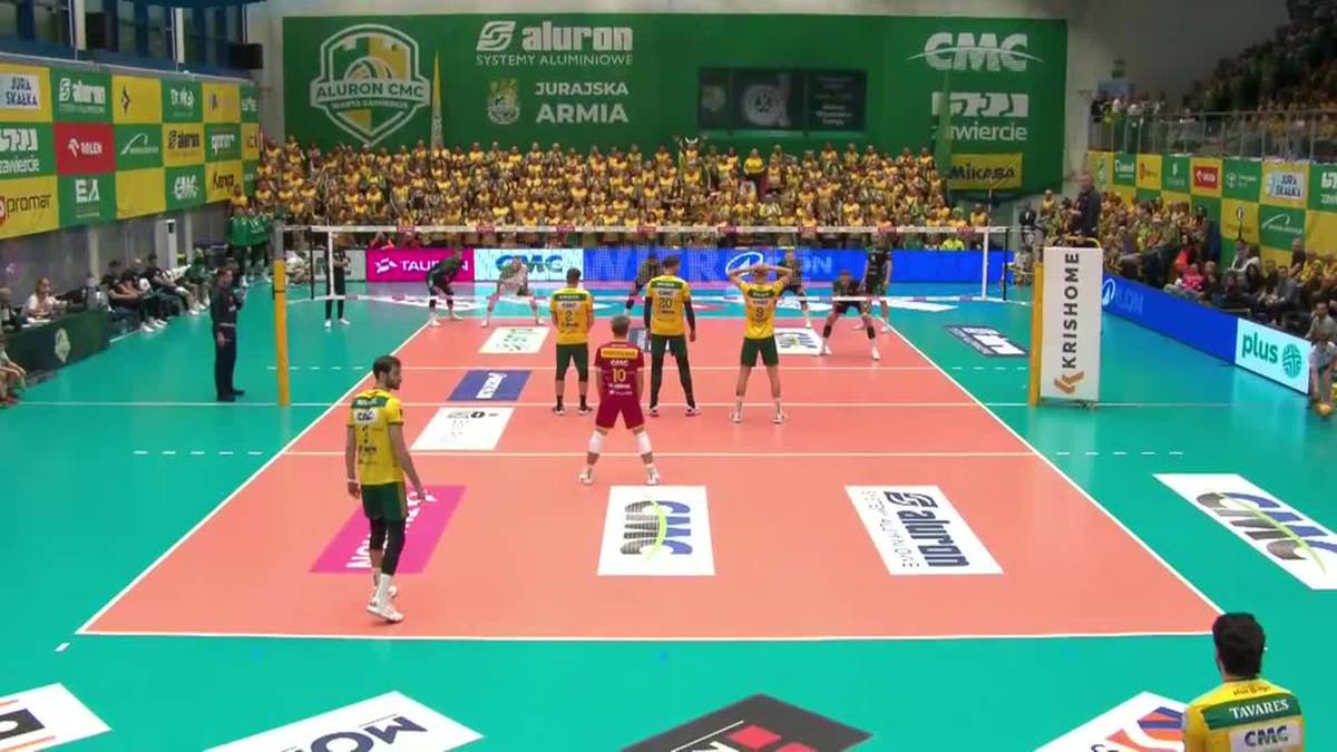 Mecz siatkówki z graczami na boisku i kibicami na trybunach.