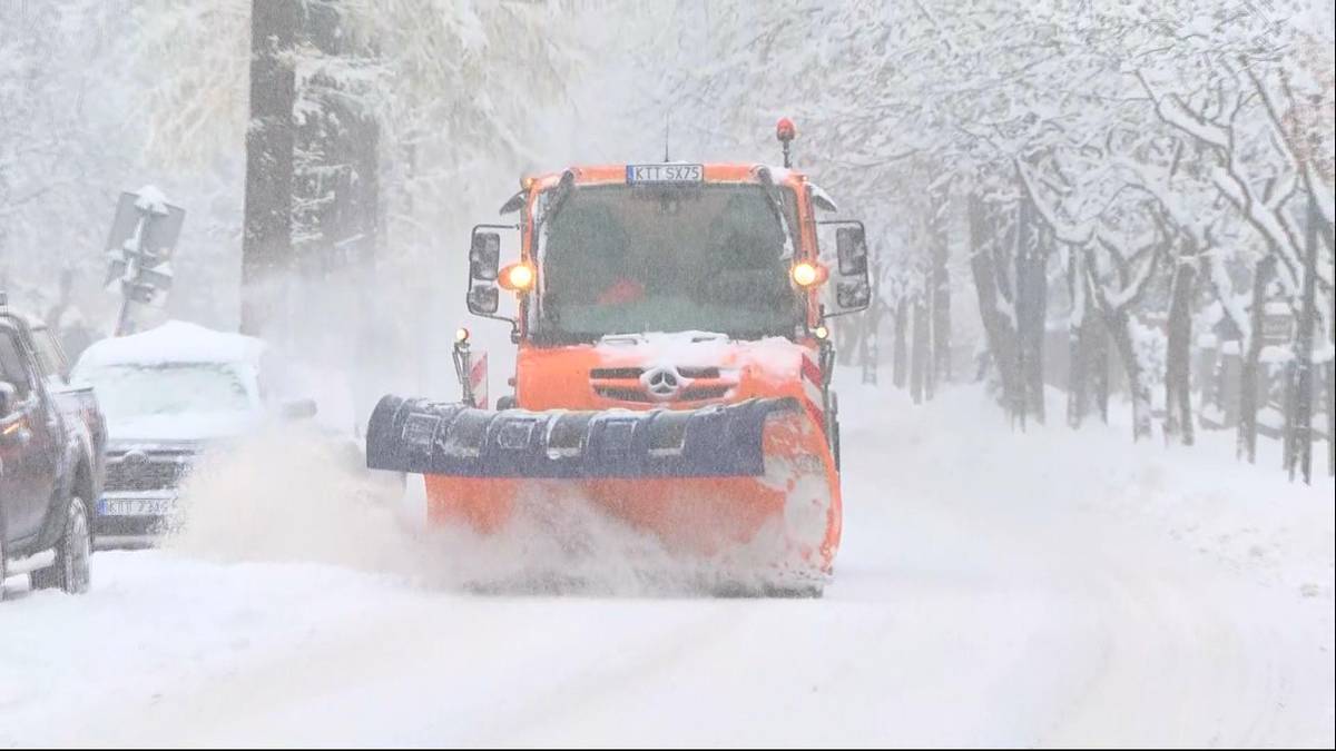 Pomarańczowy pług śnieżny z łyżką odśnieżającą na zaśnieżonej drodze podczas opadów śniegu.