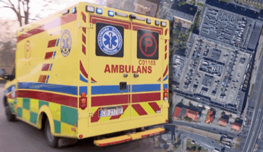 Karetka pogotowia z napisem "AMBULANS" na tle widoku z lotu ptaka na parking galerii handlowej.