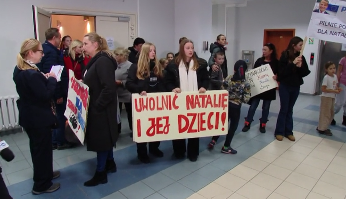 Grupa osób, w tym dzieci, trzyma transparenty z hasłami poparcia dla Natalii i jej dzieci, którzy zostali zatrzymani w Niemczech.