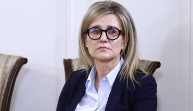 Kobieta w okularach siedzi na krześle, trzymając dokumenty w dłoniach.