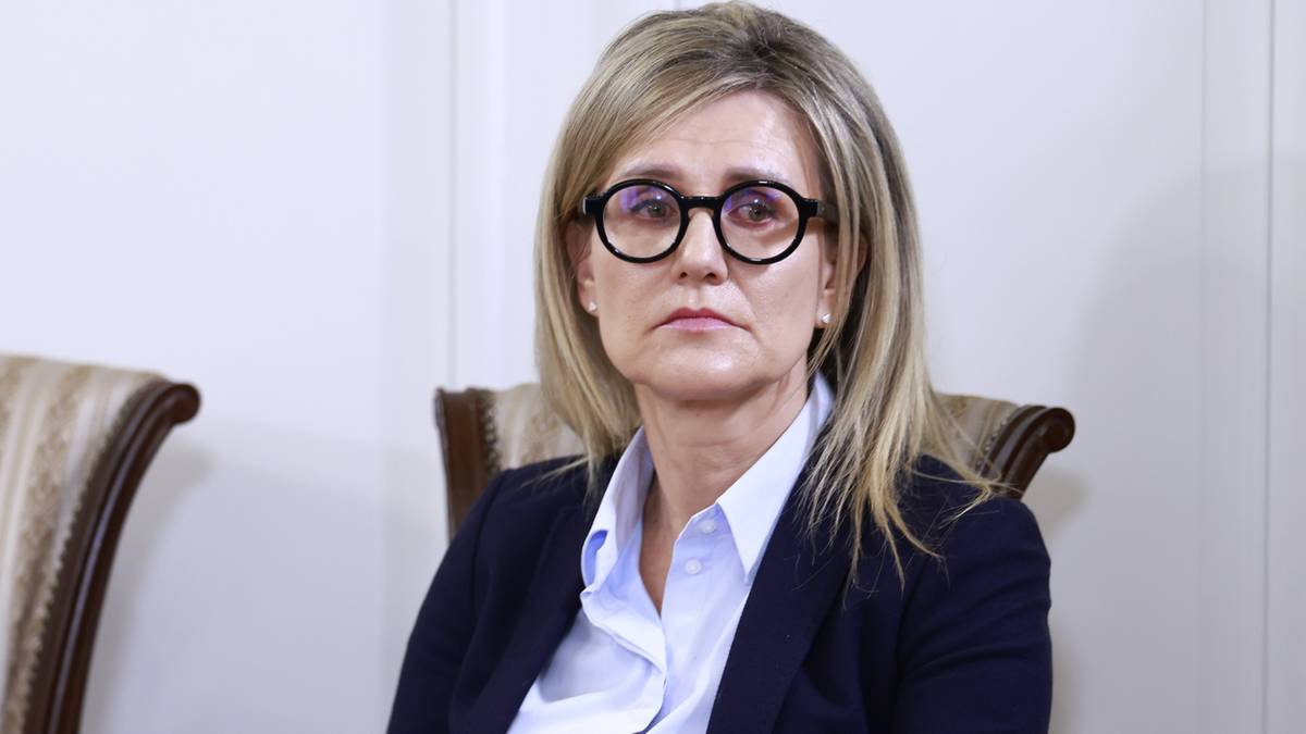 Kobieta w okularach siedzi na krześle, trzymając dokumenty w dłoniach.