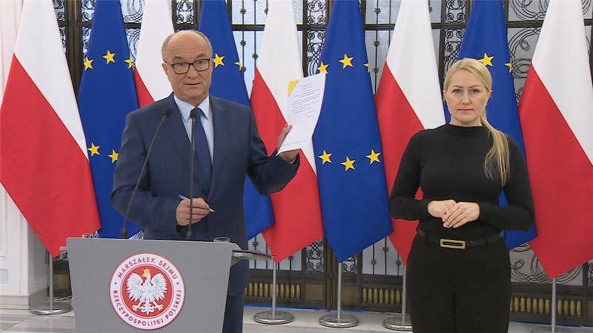 Mężczyzna w garniturze i kobieta w czarnym stroju stoją za mównicą na tle flag Polski i Unii Europejskiej.