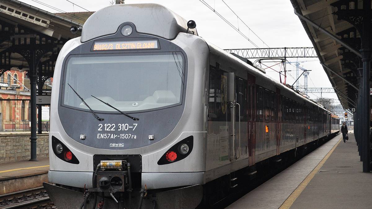 Srebrno-szary pociąg z numerem 2122 310-7 stoi na peronie dworca kolejowego.