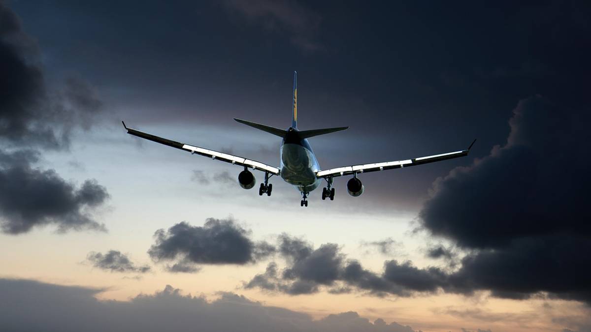 Widok od tyłu na samolot pasażerski w locie, na tle ciemnych, burzowych chmur o zachodzie słońca.