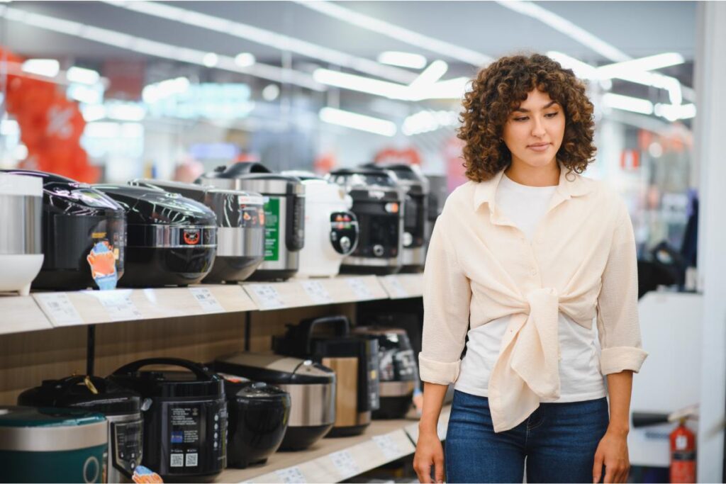 Kobieta stojąca przed półką z różnymi modelami multicookerów w sklepie AGD