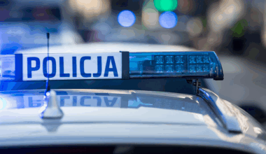 Fragment radiowozu policyjnego z włączonymi niebieskimi światłami i napisem POLICJA.
