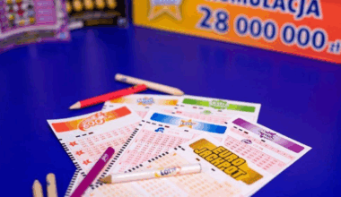 Kupony gier liczbowych Lotto i Eurojackpot na niebieskim stole, z widocznym fragmentem banera o kumulacji 28 milionów złotych.