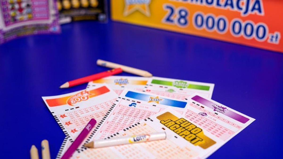 Kupony gier liczbowych Lotto i Eurojackpot na niebieskim stole, z widocznym fragmentem banera o kumulacji 28 milionów złotych.