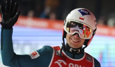 Kamil Stoch w kasku i okularach narciarskich pozdrawia, machając ręką.