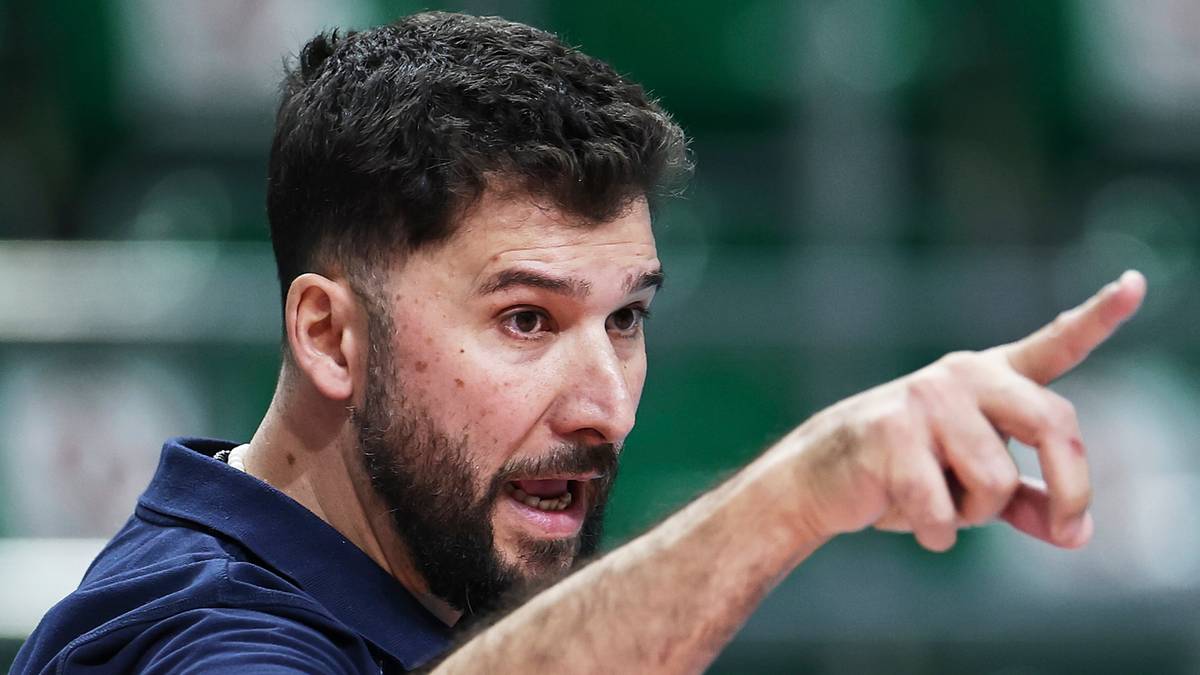 Mężczyzna w granatowej koszulce wskazuje palcem na coś poza kadrem.