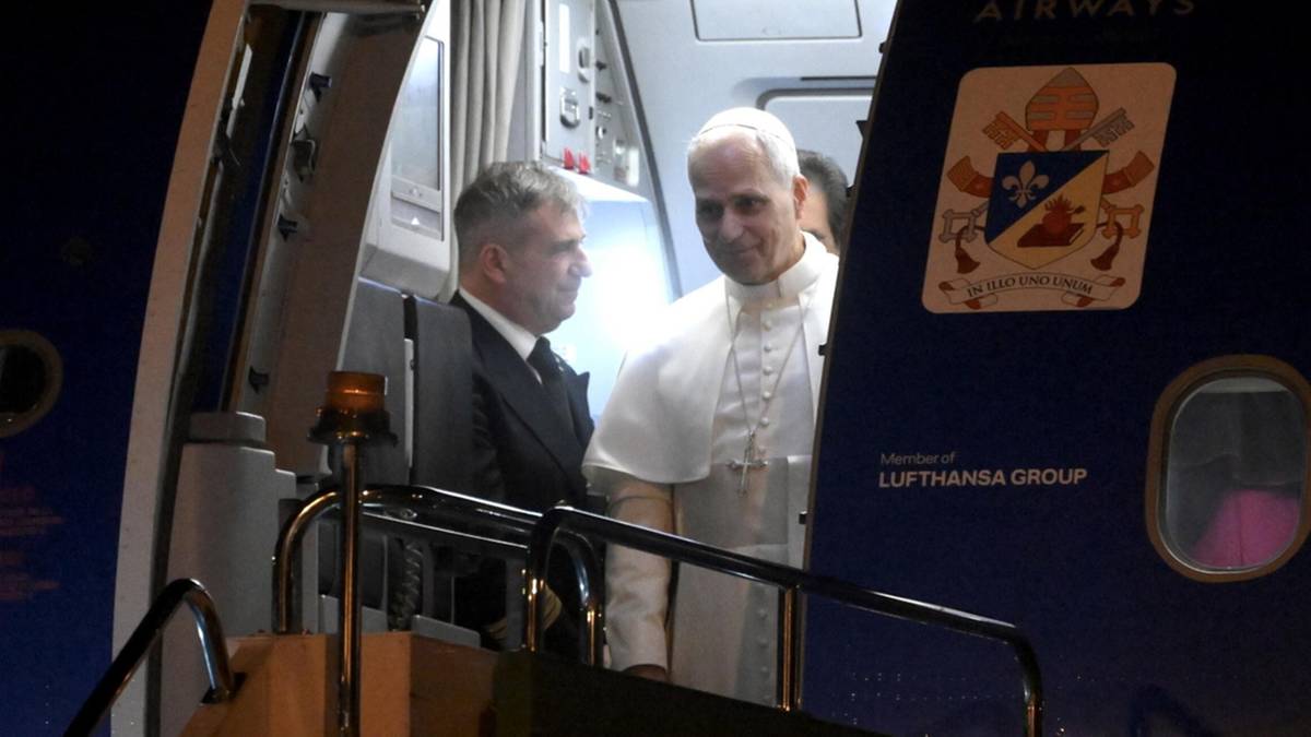 Papież Leon XIV w białej szacie wchodzi po schodach samolotu, obok niego stoi mężczyzna w garniturze.