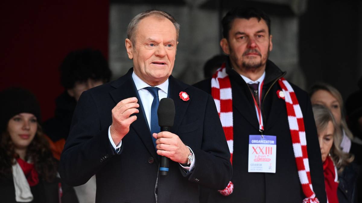 Premier Donald Tusk przemawia na tle grupy osób, trzymając mikrofon.