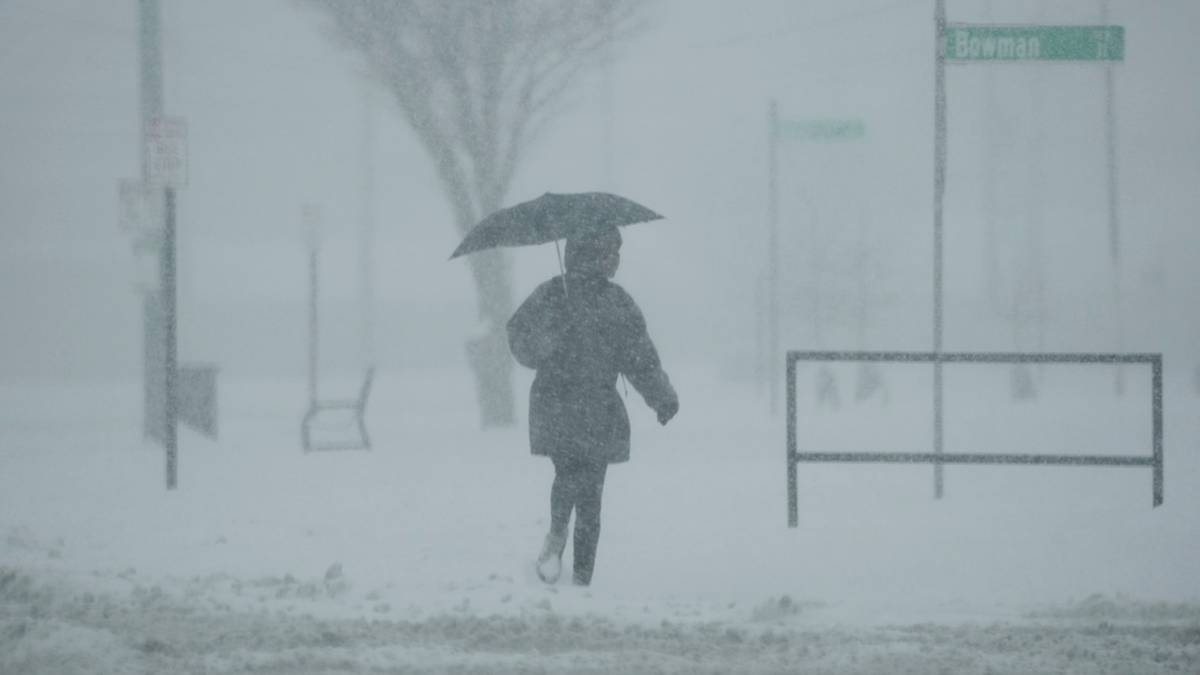 Osoba z parasolką idąca przez zaśnieżoną ulicę podczas silnych opadów śniegu, widoczność jest ograniczona.