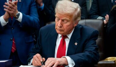 Donald Trump podpisuje dokument, obok stoją inni mężczyźni.