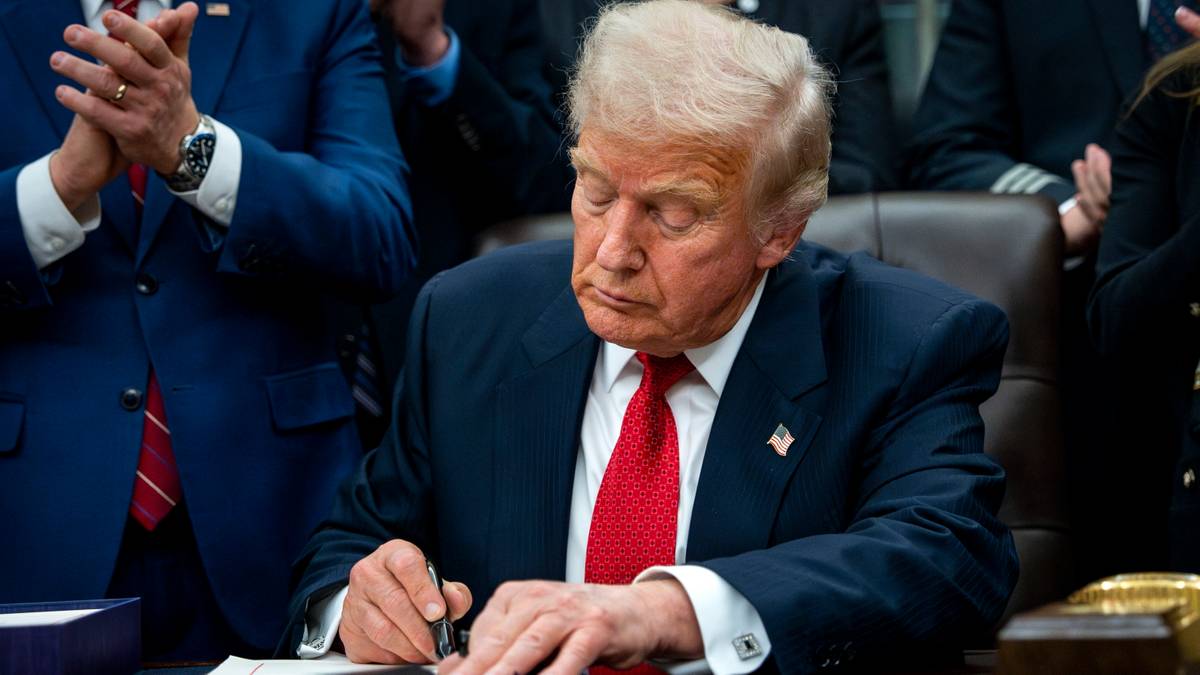 Donald Trump podpisuje dokument, obok stoją inni mężczyźni.