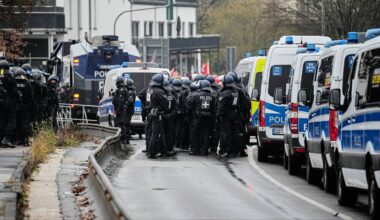 Grupa policjantów w pełnym rynsztunku stoi w rzędzie obok policyjnych radiowozów i pojazdów.