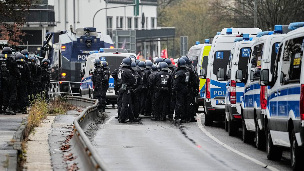 Grupa policjantów w pełnym rynsztunku stoi w rzędzie obok policyjnych radiowozów i pojazdów.