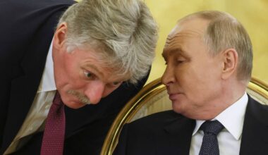 Dwaj mężczyźni w garniturach, jeden pochylony i mówiący, drugi słuchający.