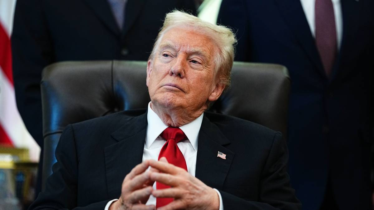 Donald Trump siedzący za biurkiem w garniturze, z dłońmi złożonymi przed sobą.