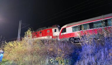 Dwa zderzone pociągi pasażerskie stoją obok siebie na tle nocnego krajobrazu z krzewami i liniami energetycznymi.