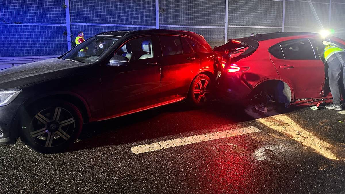 Widok na nocny karambol na trasie S2. Dwa samochody osobowe, jeden czerwony i jeden ciemny, stoją na drodze, z widocznymi uszkodzeniami. W tle znajdują się bariery dźwiękochłonne i światła pojazdów ratowniczych.