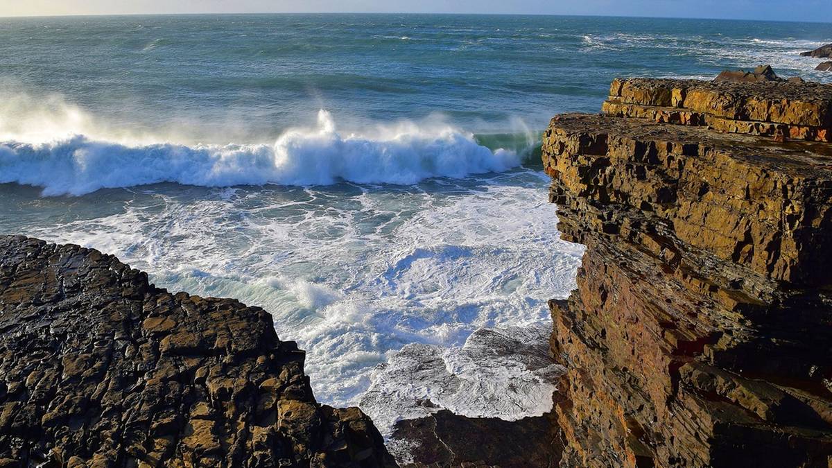 Skaliste wybrzeże Kalifornii z wielkimi, spienionymi falami rozbijającymi się o klify.