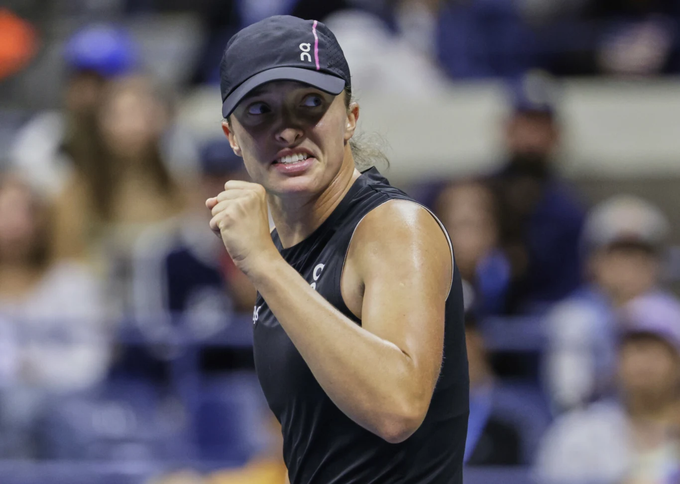 Zdeterminowana tenisistka w czarnej czapce i stroju sportowym świętuje zwycięstwo z zaciśniętą pięścią na tle widowni.