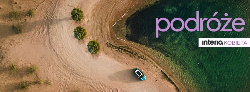 Plaża z piaskiem i kilkoma drzewami, pojedynczy samochód zaparkowany blisko brzegu zielonego jeziora, widok z lotu ptaka, typowa scena podróżnicza.