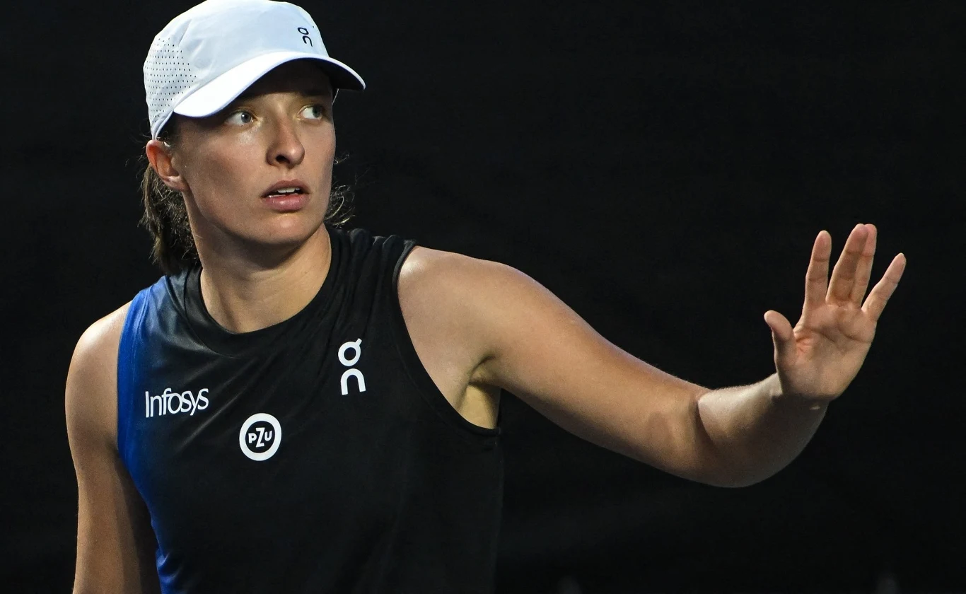 Tenisistka w sportowym stroju oraz czapce z daszkiem wykonuje gest ręką na ciemnym tle, skupiona na grze.