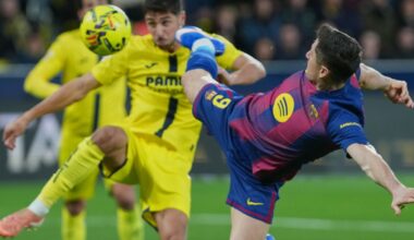 Dwóch piłkarzy rywalizuje o piłkę podczas meczu. Jeden z zawodników ubrany w żółty strój znajduje się w powietrzu ponad pochylonym przeciwnikiem w niebiesko-bordowym stroju.