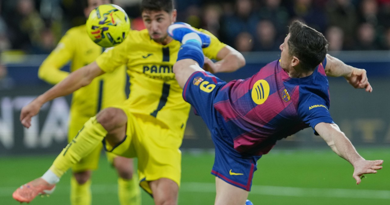 Dwóch piłkarzy rywalizuje o piłkę podczas meczu. Jeden z zawodników ubrany w żółty strój znajduje się w powietrzu ponad pochylonym przeciwnikiem w niebiesko-bordowym stroju.