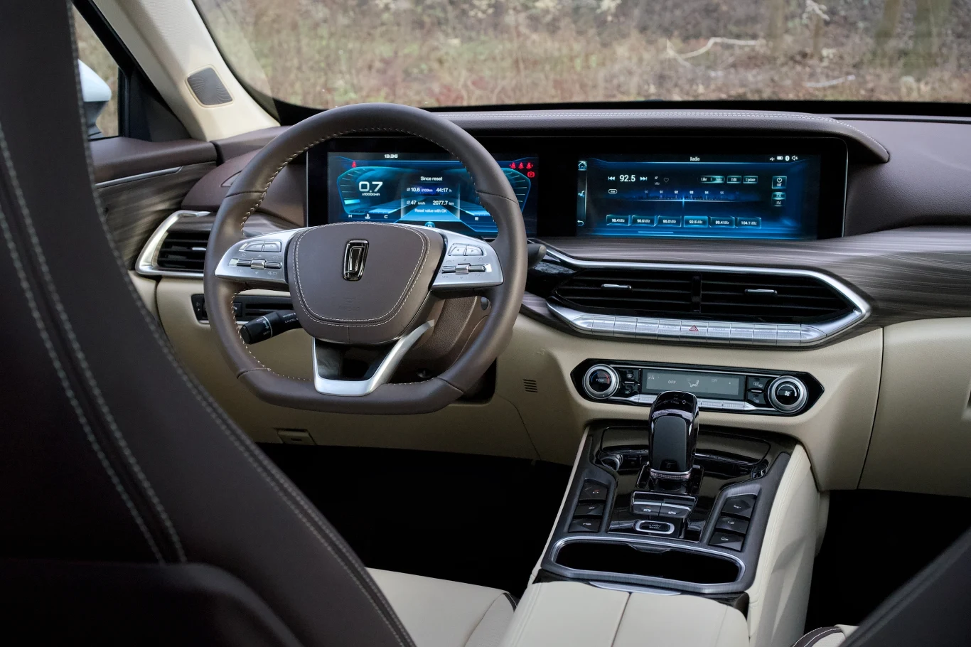 Kokpit nowoczesnego samochodu z elektroniczną deską rozdzielczą, dużym ekranem dotykowym, luksusową kierownicą oraz jasną, skórzaną tapicerką. Wnętrze prezentuje wysoką jakość wykończenia i zaawansowane technologie.