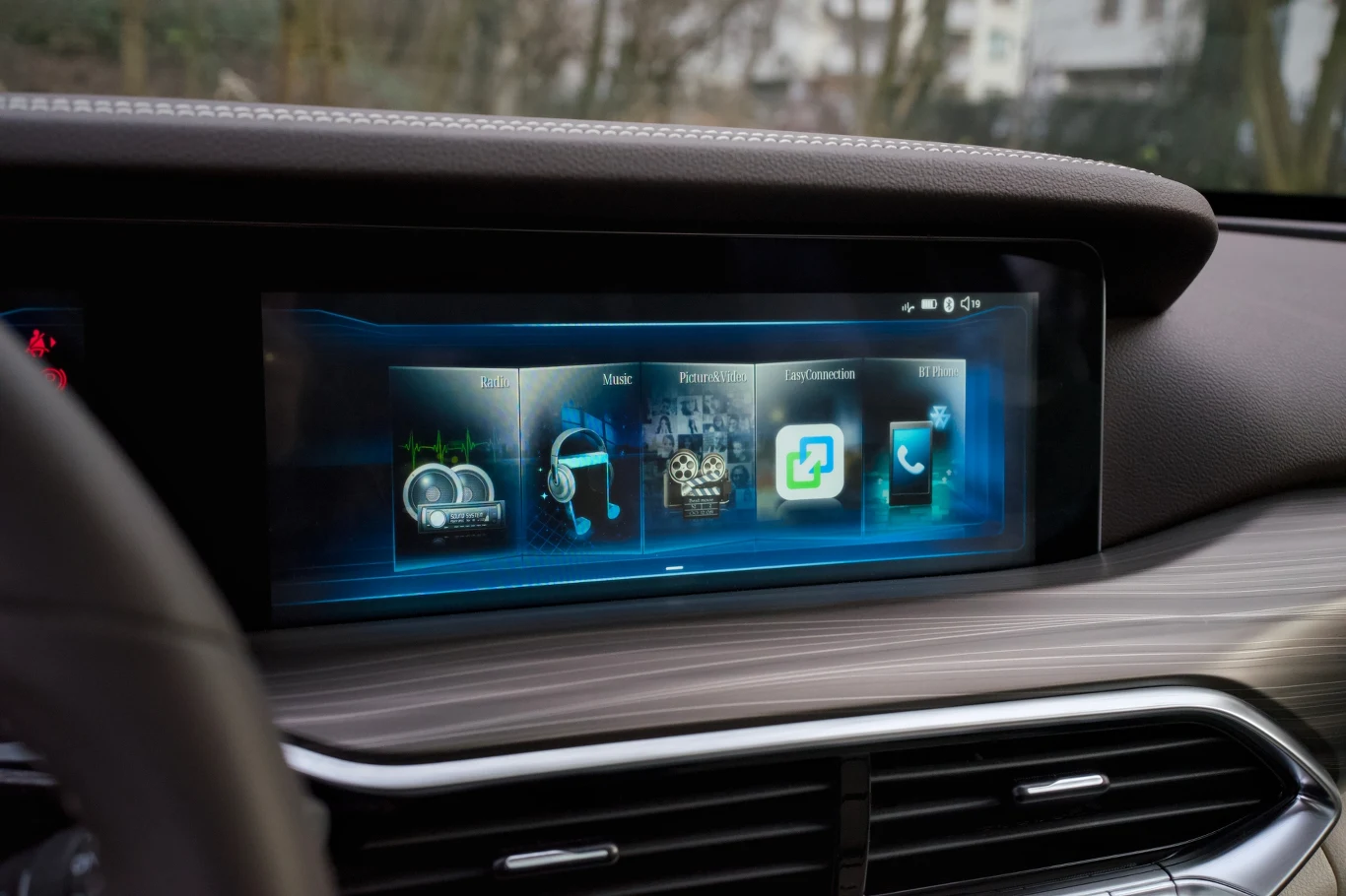 Nowoczesny ekran dotykowy w samochodzie wyświetlający menu multimedialne z ikonami nawigacji, muzyki, ustawień systemowych oraz połączeń telefonicznych, otoczony eleganckim panelem z drewna i stalowymi akcentami.