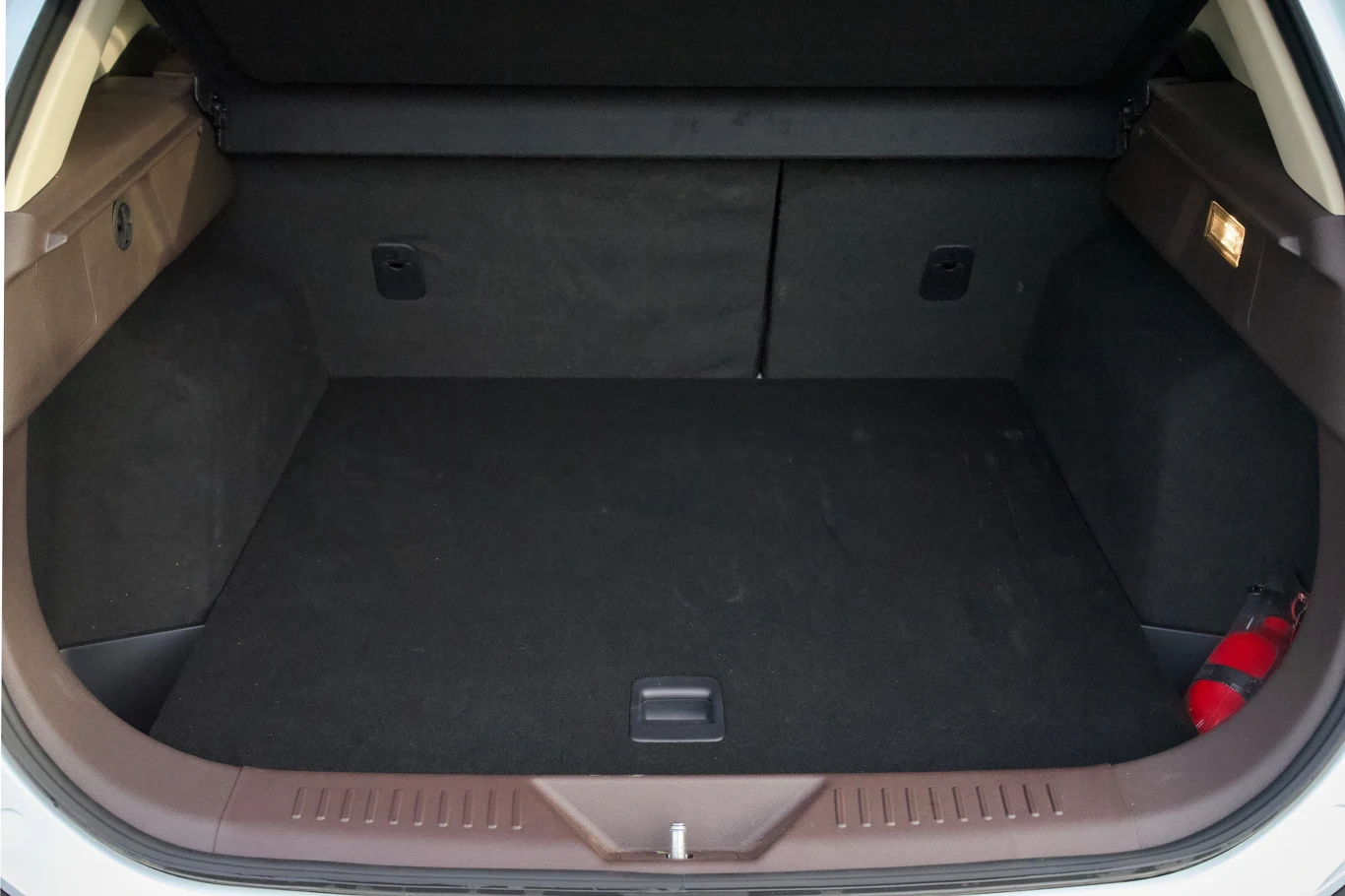Pojemny bagażnik samochodu wyłożony ciemną wykładziną, po prawej stronie widoczna gaśnica zamocowana do ściany bagażnika, po lewej stronie kieszeń oraz światło oświetlające wnętrze.