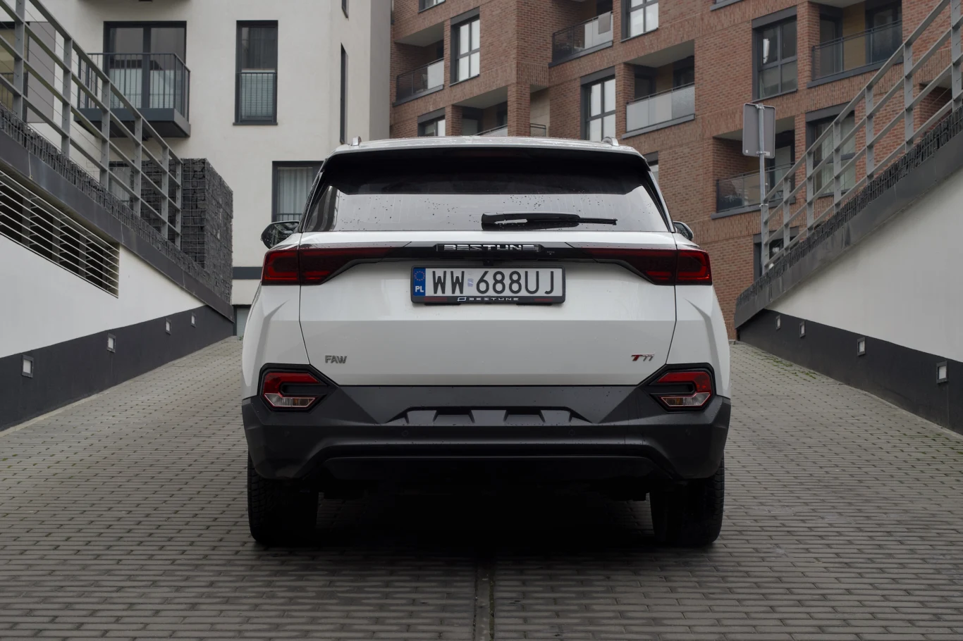 Biały samochód osobowy stojący tyłem na kostce brukowej pomiędzy nowoczesnymi budynkami mieszkalnymi. Na pojeździe widoczna polska tablica rejestracyjna, LED-owe tylne lampy i logo marki.