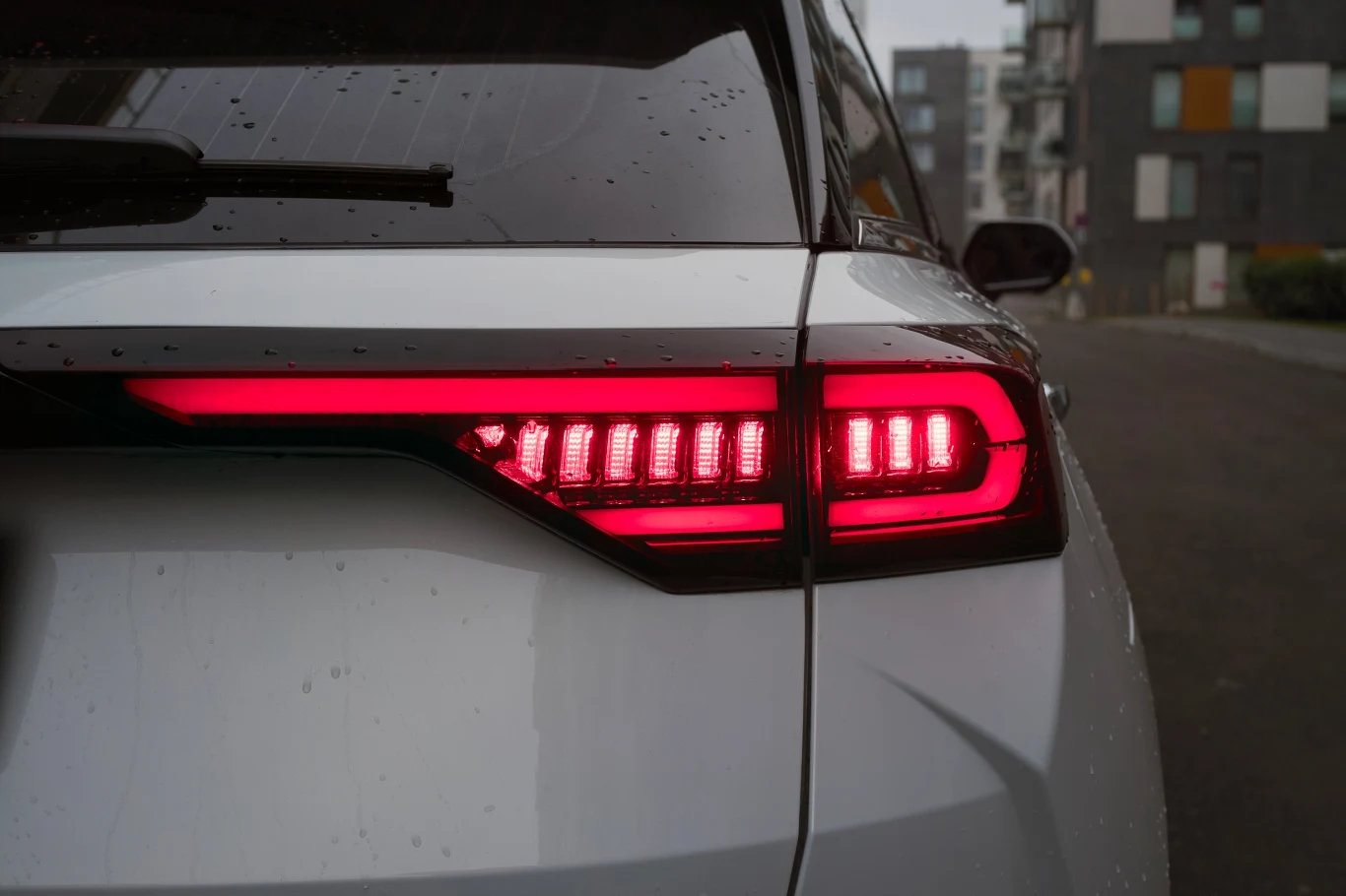 Tylna część samochodu z nowoczesnym, włączonym światłem LED w kolorze czerwonym, widoczna w miejskim otoczeniu z rozmytym tłem budynków.