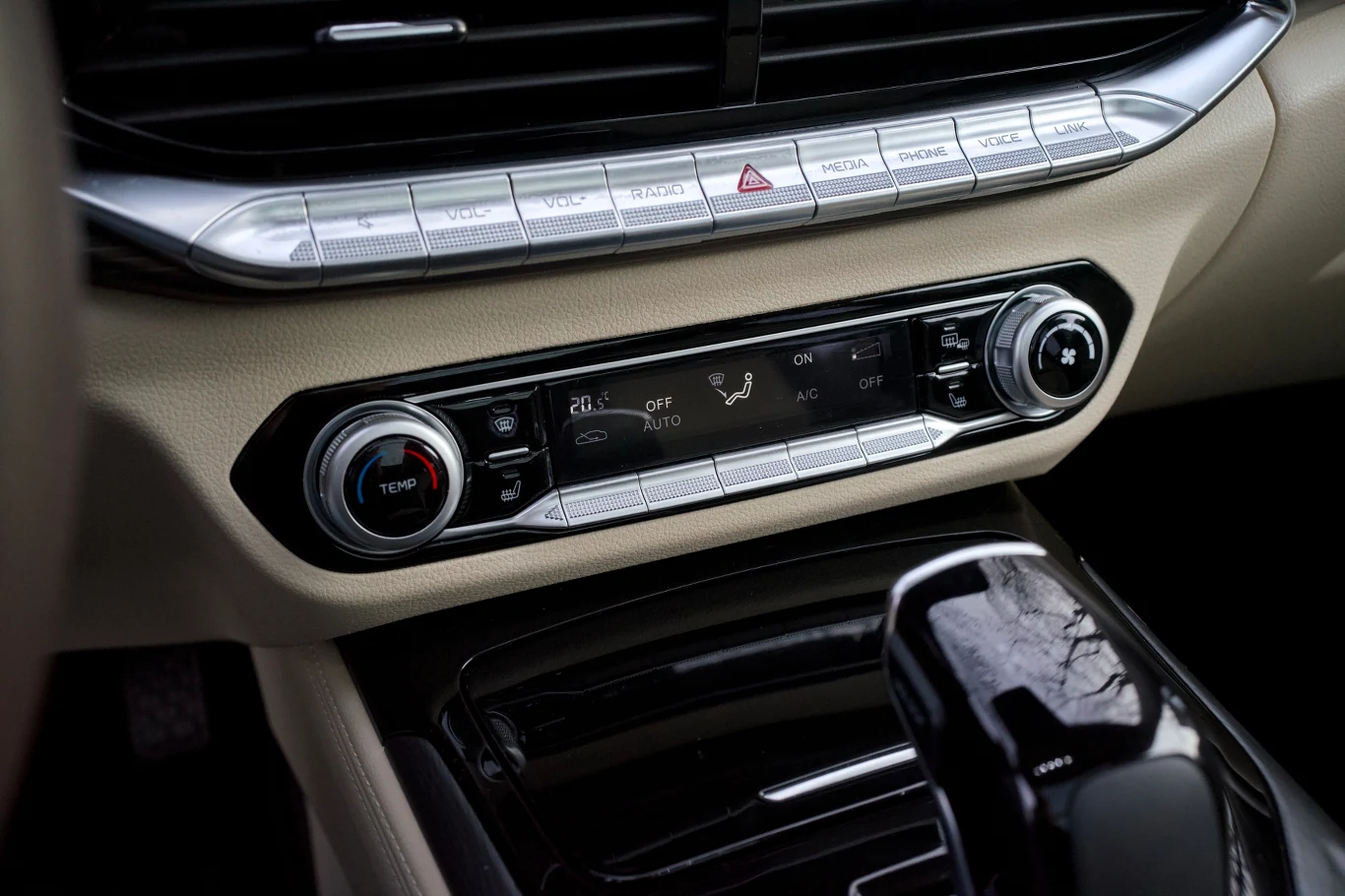 Konsola środkowa samochodu z panelem sterowania klimatyzacją, przyciskami do ustawień wentylacji, pokrętłami do regulacji temperatury oraz fragmentem dźwigni zmiany biegów.