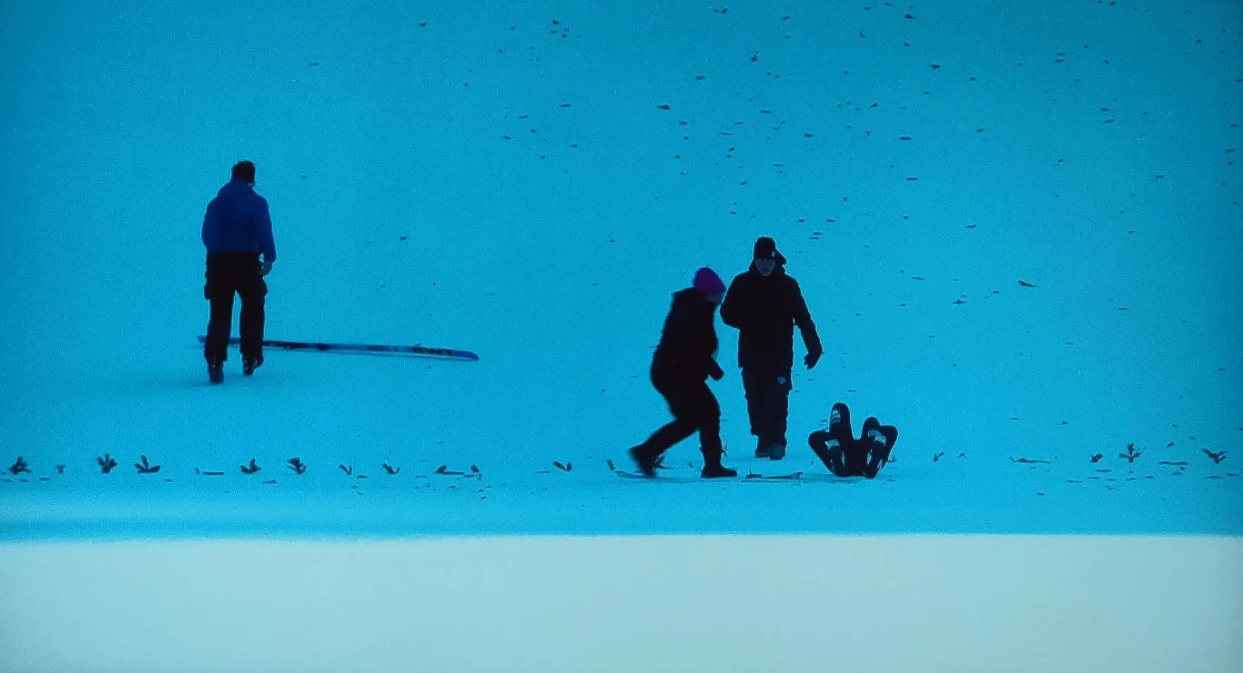 Upadek Artti Aigro Trzy osoby spacerują po śnieżnym zboczu, jedna osoba leży na plecach na śniegu, całość utrzymana w niebieskiej tonacji.