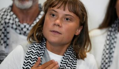 Greta Thunberg w białej koszulce i szaliku w czarno-białe wzory.