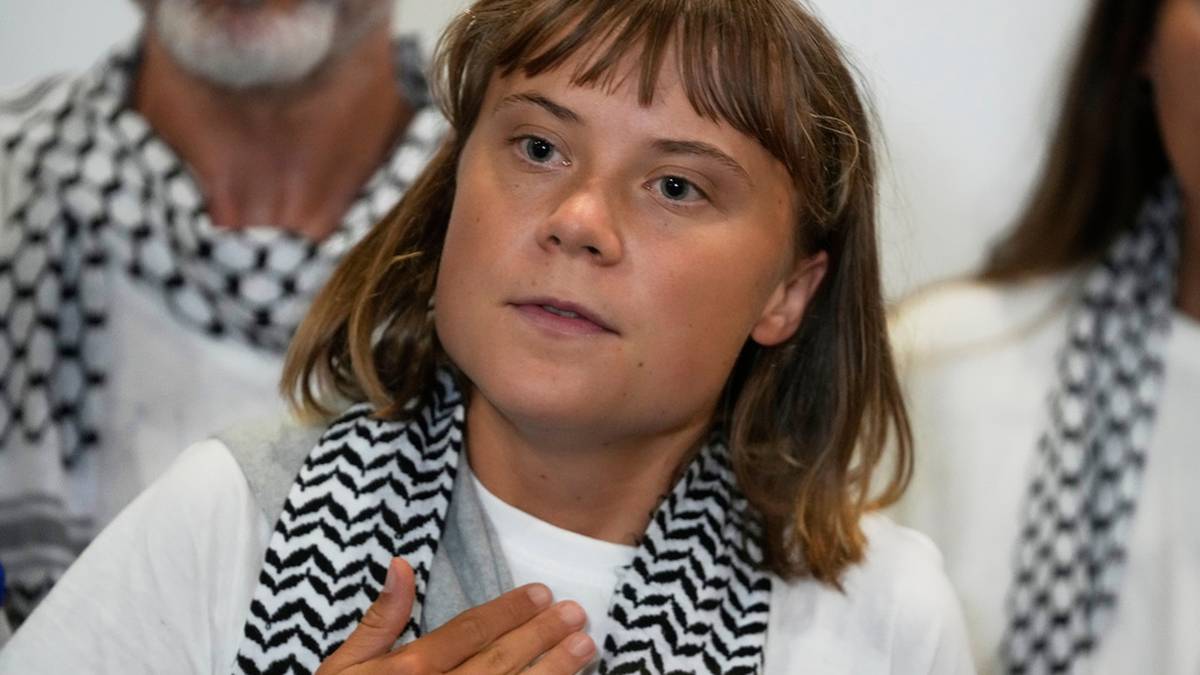Greta Thunberg w białej koszulce i szaliku w czarno-białe wzory.