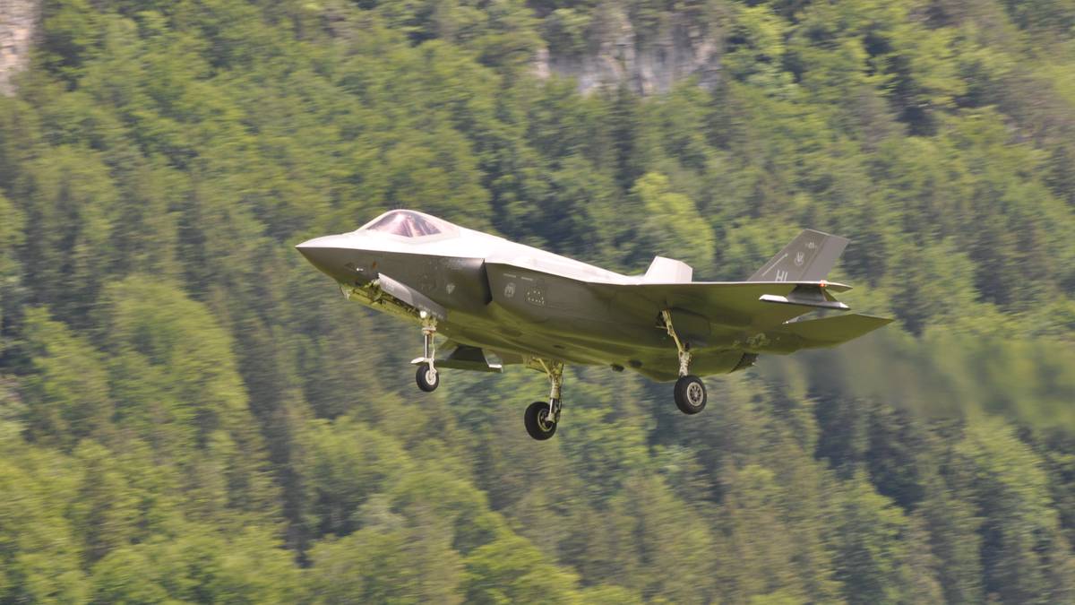 Nowoczesny myśliwiec F-35A podczas lotu na tle zalesionego wzg&oacute;rza.