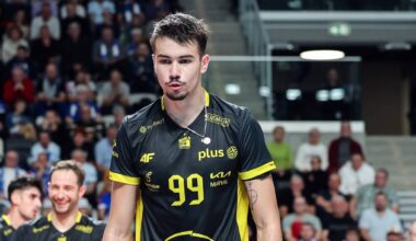 Siatkarz z numerem 99 na koszulce prowadzi drużynę na boisko, w tle kibice na trybunach.