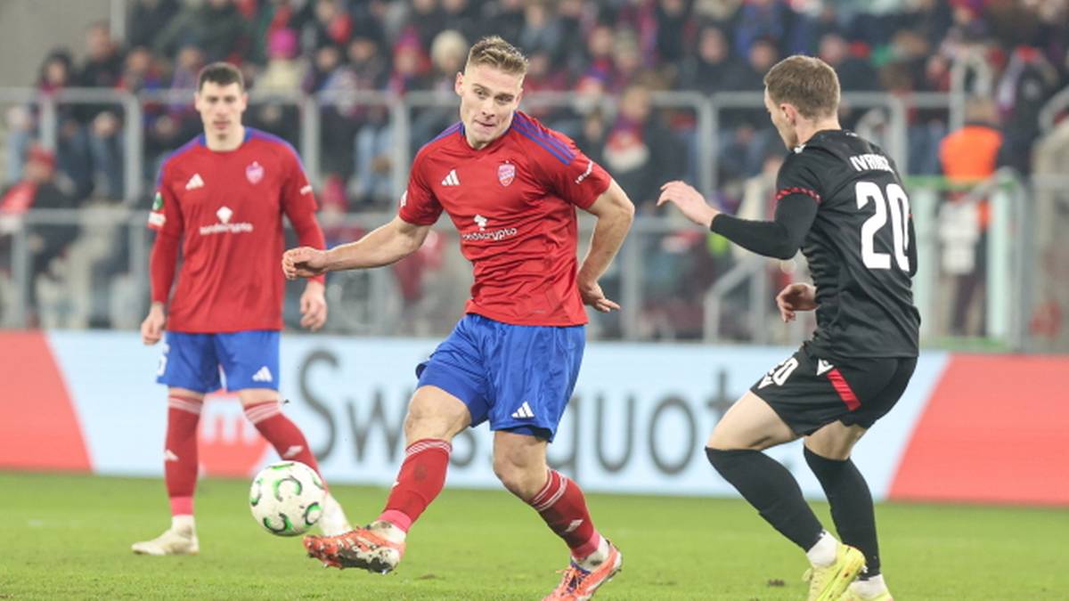 Piłkarz w czerwonej koszulce z niebieskimi spodenkami pr&oacute;buje odebrać piłkę zawodnikowi w czarnej koszulce.