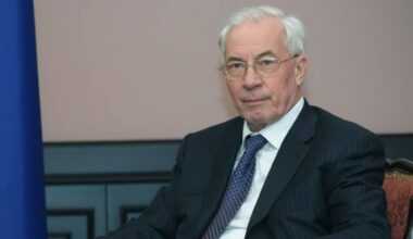 Portret starszego mężczyzny w garniturze i krawacie, siedzącego i patrzącego w obiektyw.