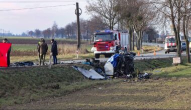Miejsce wypadku drogowego z widocznym wrakiem samochodu, strażą pożarną i innymi pojazdami.