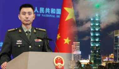 Oficer w mundurze wojskowym stojący przy m&oacute;wnicy na tle flagi Chin i panoramy miasta.