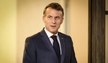 Emmanuel Macron w ciemnym garniturze i białej koszuli z krawatem, lekko uśmiechnięty.