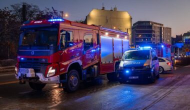 Samoch&oacute;d strażacki i radiow&oacute;z policyjny stojące na ulicy w nocy, oba pojazdy mają włączone niebieskie światła ostrzegawcze.